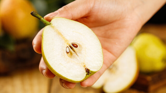 Fruit closeup shows hand holding a sliced pear with seeds exposed in a kitchen setting