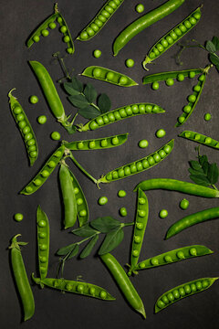 Fresh bright green pea pods pattern on charcoal black textured background.