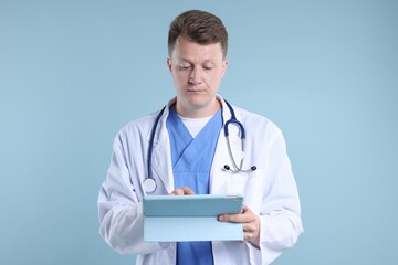 Fototapeta premium Doctor with stethoscope using tablet on light blue background