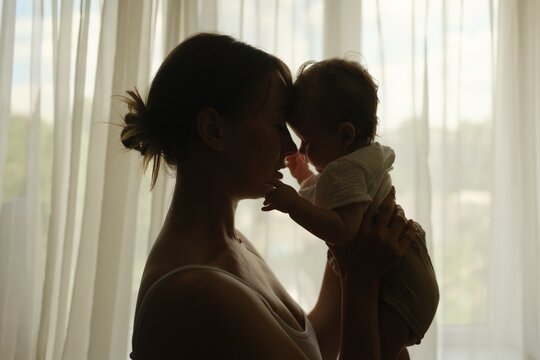 ilhouette of a mother lifting her baby up in front of a window, cozy home atmosphere