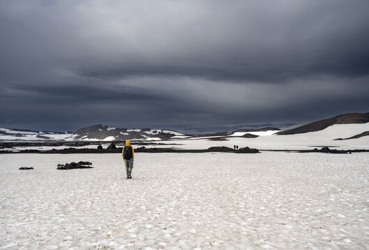 Hikers in snow-covered volcanic landscape with volcanic sand and petrified lava, crater of Askja volcano, Icelandic highlands, Iceland