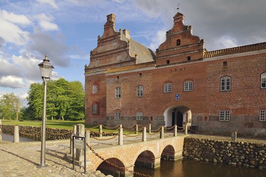 Historic brick castle with bridge over a moat on a cloudy day, Broholm, manor house route, Funen, Denmark