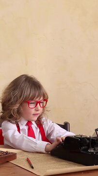Funny kid pretending to be a businessman. A little child is playing in the office with a vintage typewriter and a retro telephone. Vertical video, slow motion