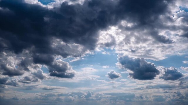 Timelapse reveals dynamic layers of clouds moving across a vibrant blue sky with bright sun rays piercing through. The dramatic heavenly spectacle highlights light and shadow.