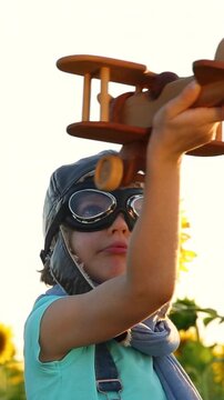 A happy child is playing with a vintage wooden airplane outside in autumn. A kid is having fun outdoors in a field of sunflowers. The concept of imagination and freedom. Vertical video, slow motion