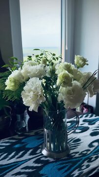 Beautiful eustoma flowers and tender roses bouquet in glass vase on ikat pattern tablecloth. Premium oak board background, elegant lisianthus blossom, luxury apartment home interior decoration.