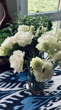 Beautiful eustoma flowers and tender roses bouquet in glass vase on ikat pattern tablecloth. Premium oak board background, elegant lisianthus blossom, luxury apartment home interior decoration.