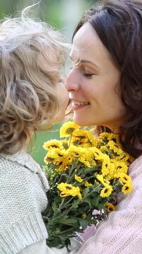 A little girl gives a beautiful woman a bouquet of autumn flowers in the park. Mom and daughter have fun in the autumn park. Vertical video, slow motion