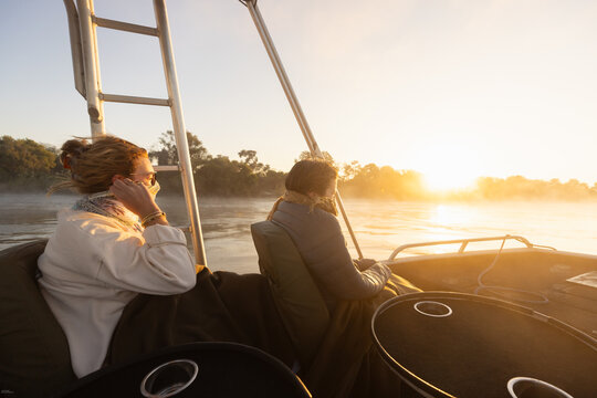  young people experiencing cold sunrise on the Zambezi River, as fog rises from the water, Zimbabwe, Africa