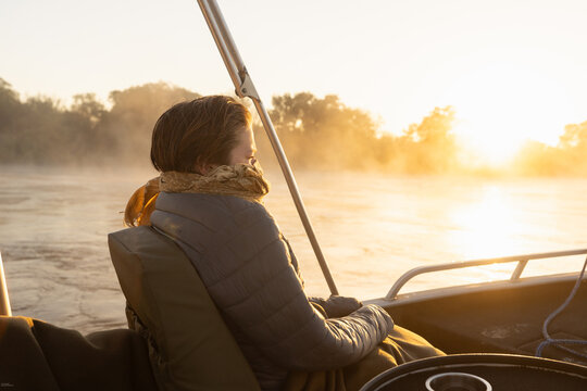  young people experiencing cold sunrise on the Zambezi River, as fog rises from the water, Zimbabwe, Africa