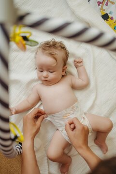 Mother hands changing diaper for her cute little baby lying on white blanket at home. Commercial lifestyle