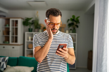 Man feeling worried seeing shocking news on smartphone at home