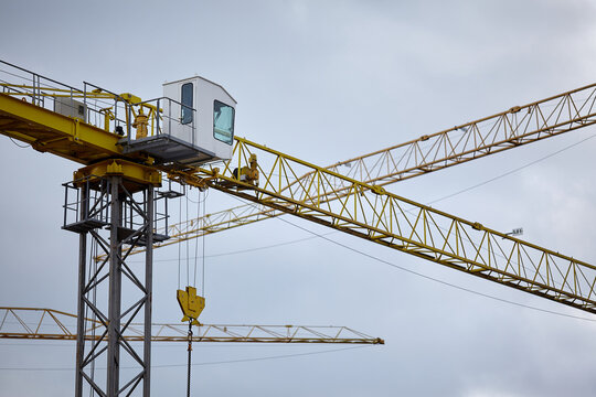 Yellow tower crane cabin and jib on construction site background. Industrial heavy machinery, building development engineering, real estate property construction process, hoisting equipment with hook 