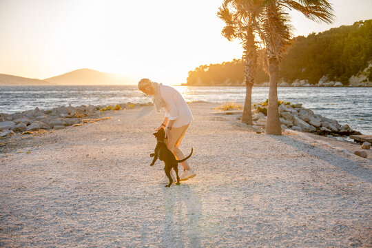 Woman playing with black Labrador retriever at sunset beach