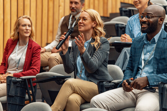 Business conference audience member asking question during panel discussion in modern auditorium
