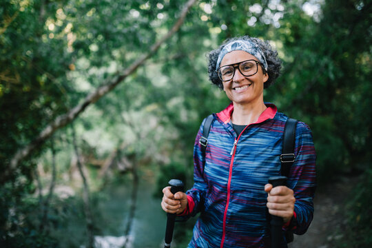 Smiling woman hiker with trekking pole in green forest