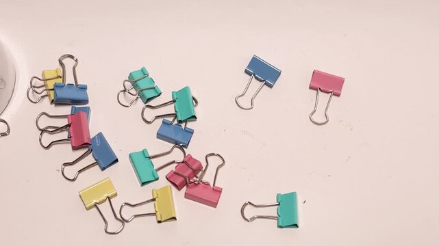 Assorted colorful binder clips falling and bouncing on a clean white office background