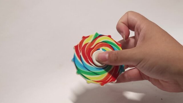 Hand holding and spinning a colorful rainbow fidget spinner toy on a white background