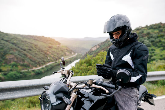Motorcyclist checking smartphone beside bike on mountain road