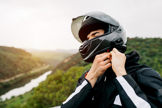 Motorcyclist fastening helmet by scenic road at sunset