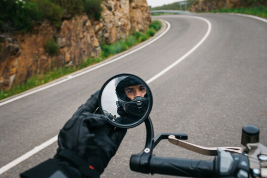 A motorcycle handlebar and mirror showing a man in a helmet