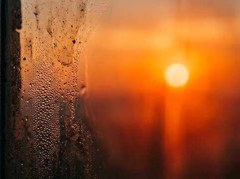 Condensation on window glass reflecting warm sunset glow during a humid summer evening atmospheric scene