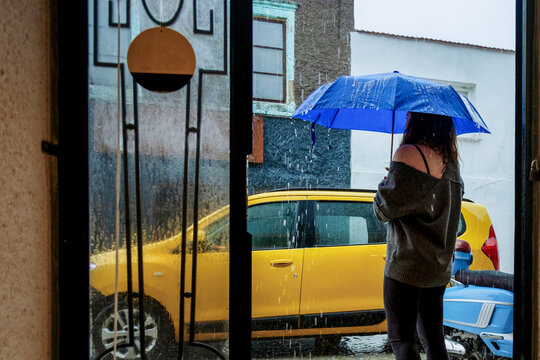 Woman with blue umbrella waiting by taxi in rainy street