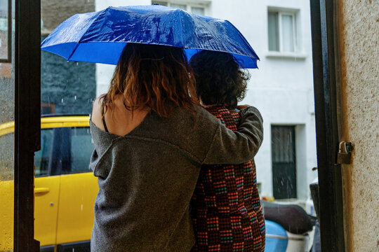 Two women share umbrella while waiting for a taxi