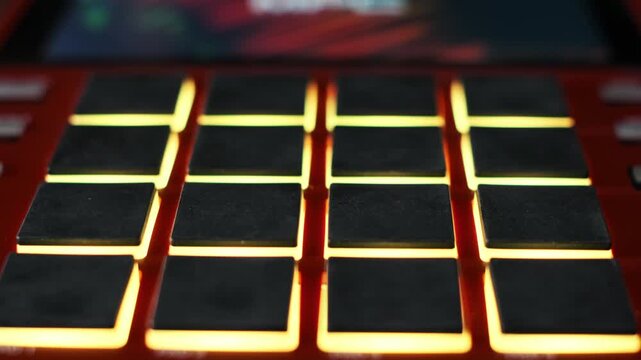 A close-up view of black rubber pads on a red drum machine illuminates with changing RGB light patterns. Concept of electronic music production, creative beat making, and modern DJ technology