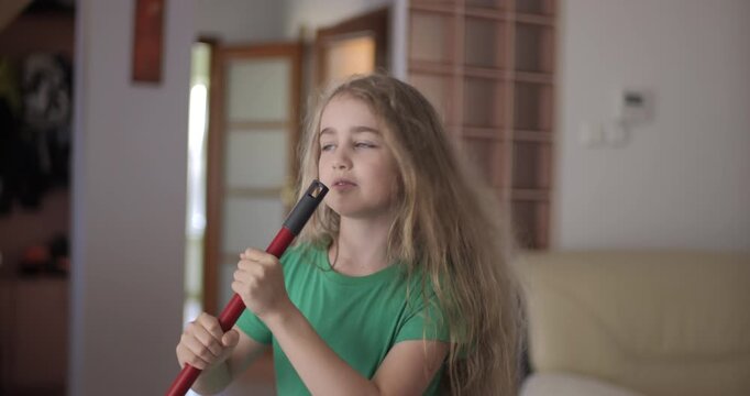 Creative Teenage Girl Singing and Using Broom Handle as Microphone. Child Using Mop as Microphone While Singing in Domestic Room. Enjoying Home Cleaning. Playful Creative Kid Dancing With Mop.