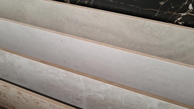 Samples of large grey and beige ceramic tiles with marble and stone textures on display in a building material store. Home renovation, interior design, flooring materials.