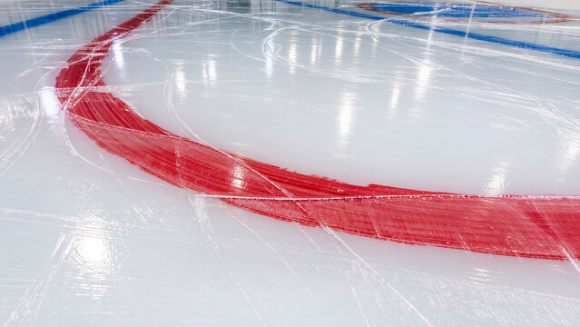 High-angle view of scratched ice rink surface with bright red line markings and visible skate blade tracks under arena lights