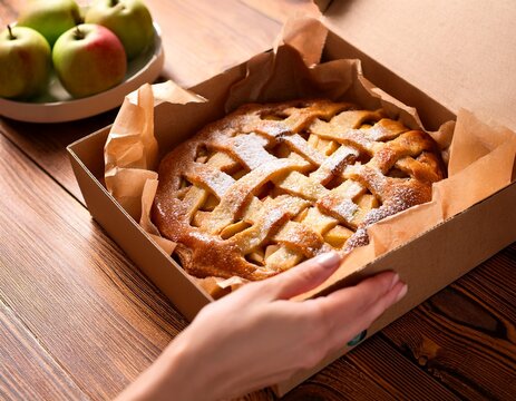 hand opening a box with an apple pie on wooden table close up