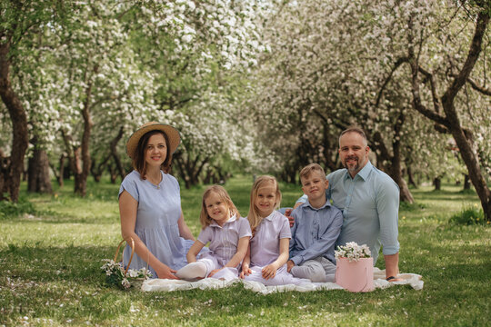 Happy family picnic under blooming orchard in springtime