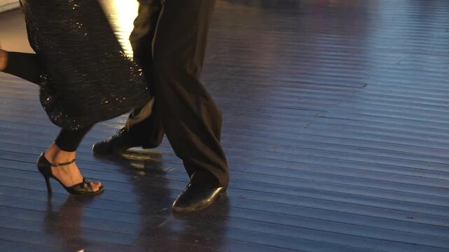 Low angle view of professional tango dancers' legs and feet. Elegant partners perform a sensual and passionate dance on a shiny wooden floor