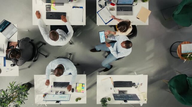 Close overhead framing follows corporate workers in corporate workspace as they are evaluating market research, using performance metrics, corporate targets and report writing in the workflow.