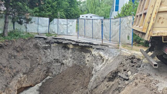 Stationary wide shot of a deep excavation pit on urban street with collapsed asphalt next to parked dump truck