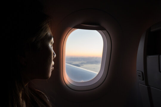 Woman gazing out airplane window at dawn above clouds