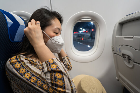 Woman wearing face mask on airplane seat by window