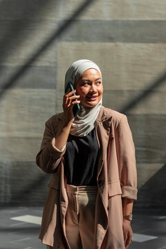 Young Muslim professional woman on phone in city sunlight