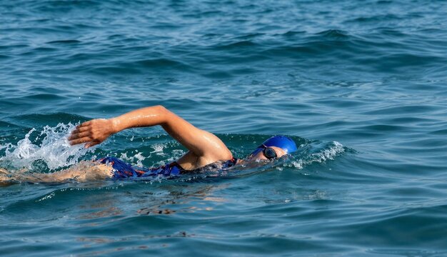 Swimmer in blue cap and goggles performing freestyle stroke in open water, creating dynamic splash in deep blue sea