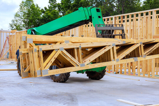 Construction workers use telehandler to lift wooden trusses at building site
