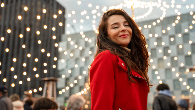 Woman in red coat smiling under Christmas city lights