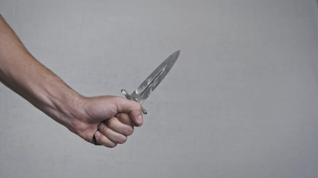 Close-up of male hands unsheathing a sharp ornate vintage dagger from its scabbard. The double-edged steel blade reflects light against a neutral background.