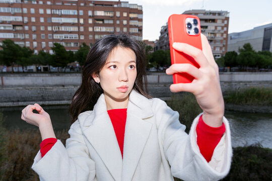 Chinese Gen Z woman taking selfie on smartphone outdoors