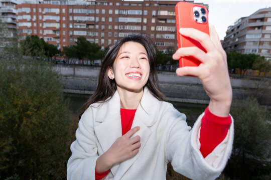 Gen Z Chinese woman taking smartphone selfie outdoors
