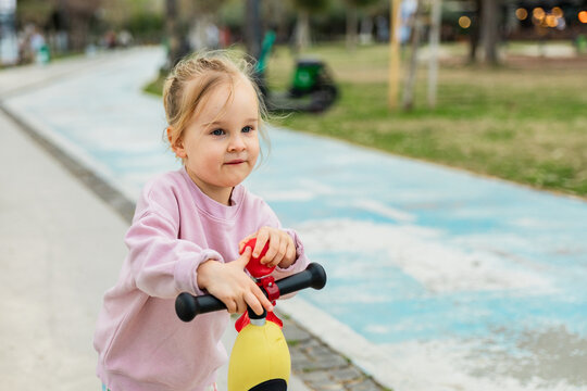 Little girl riding balance bike on park path outdoors