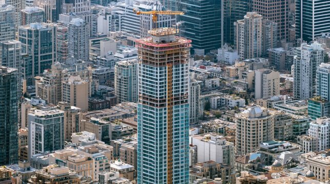 Modern skyscraper under construction with crane against a backdrop of city buildings
