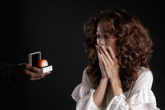 Surprised young female with curly hair receiving unusual sushi ring gift