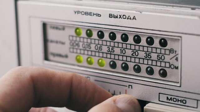 Macro shot of a hand adjusting a balance slider on a vintage audio amplifier shifting sound between channels. A blinking green LED meter shows the signal with Cyrillic text labels.